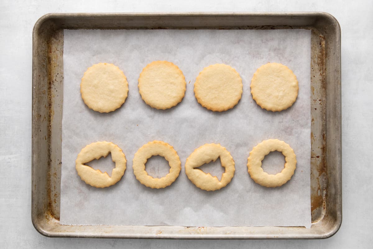 cookies lined up on a baking tray, four have Christmas shapes cut out of the middle - 11