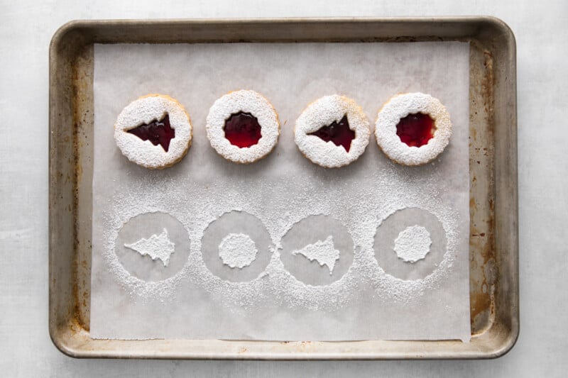 linzer cookies covered with powdered sugar lined up on a baking tray
