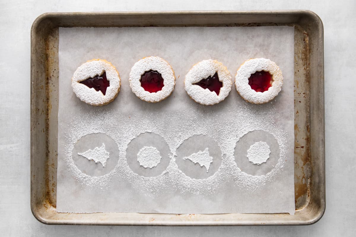 Linzer cookies covered with powdered sugar lined up on a baking tray.