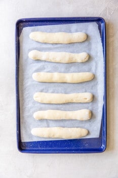 unbaked olive garden breadsticks on a blue baking sheet.