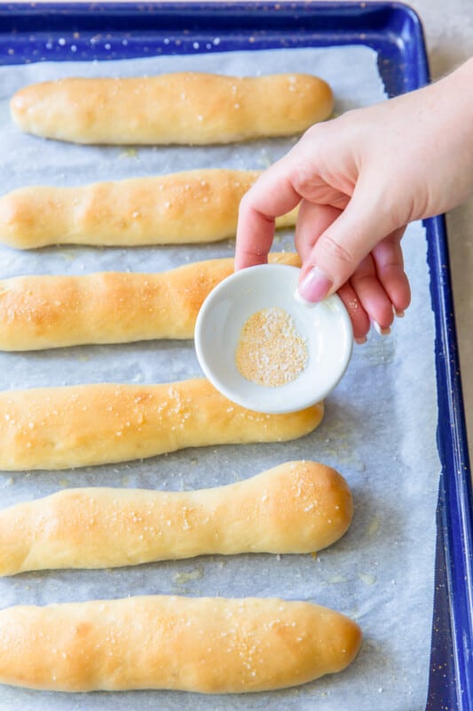 garlic salt sprinkled over olive garden breadsticks on a blue baking sheet.