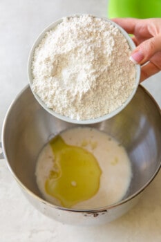 flour, salt, and olive oil added to yeast mixture in a stainless mixing bowl.