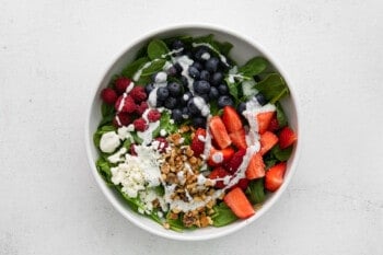poppy seed dressing drizzled over ingredients for spinach berry salad in a white bowl.