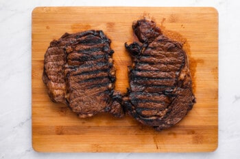 2 grilled ribeyes on a wooden cutting board.