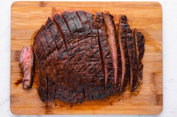 overhead view of sliced cooked flank steak on a wooden cutting board.
