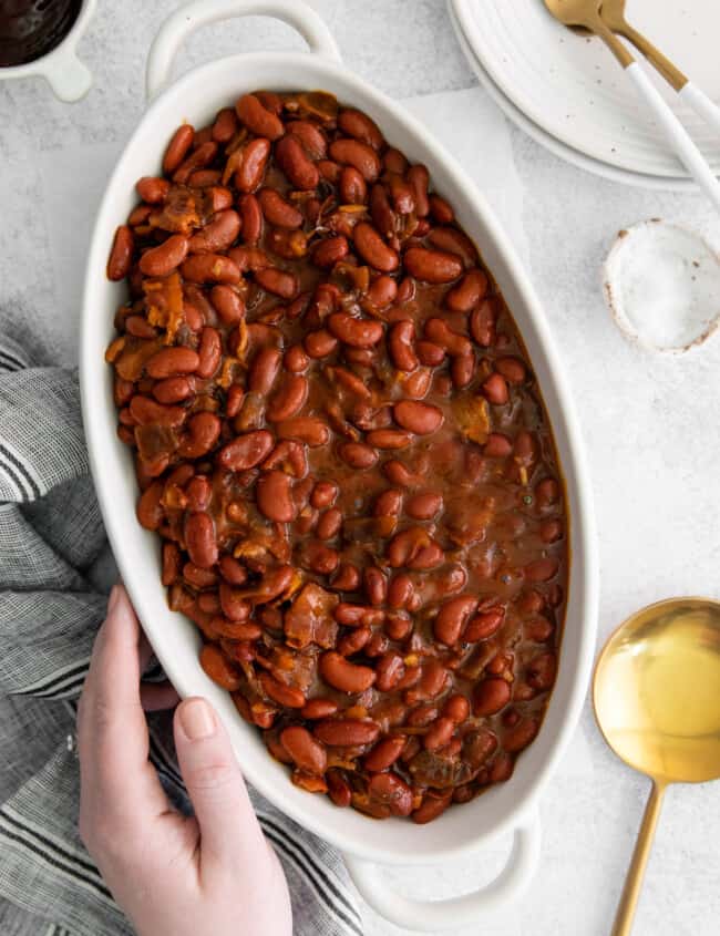overhead view of a hand grabbing a bowl of instant pot bbq baked beans.