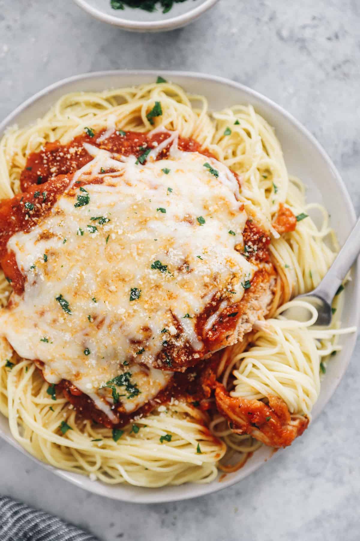 a forkful of pasta resting on a plate of pressure cooker chicken parmesan.