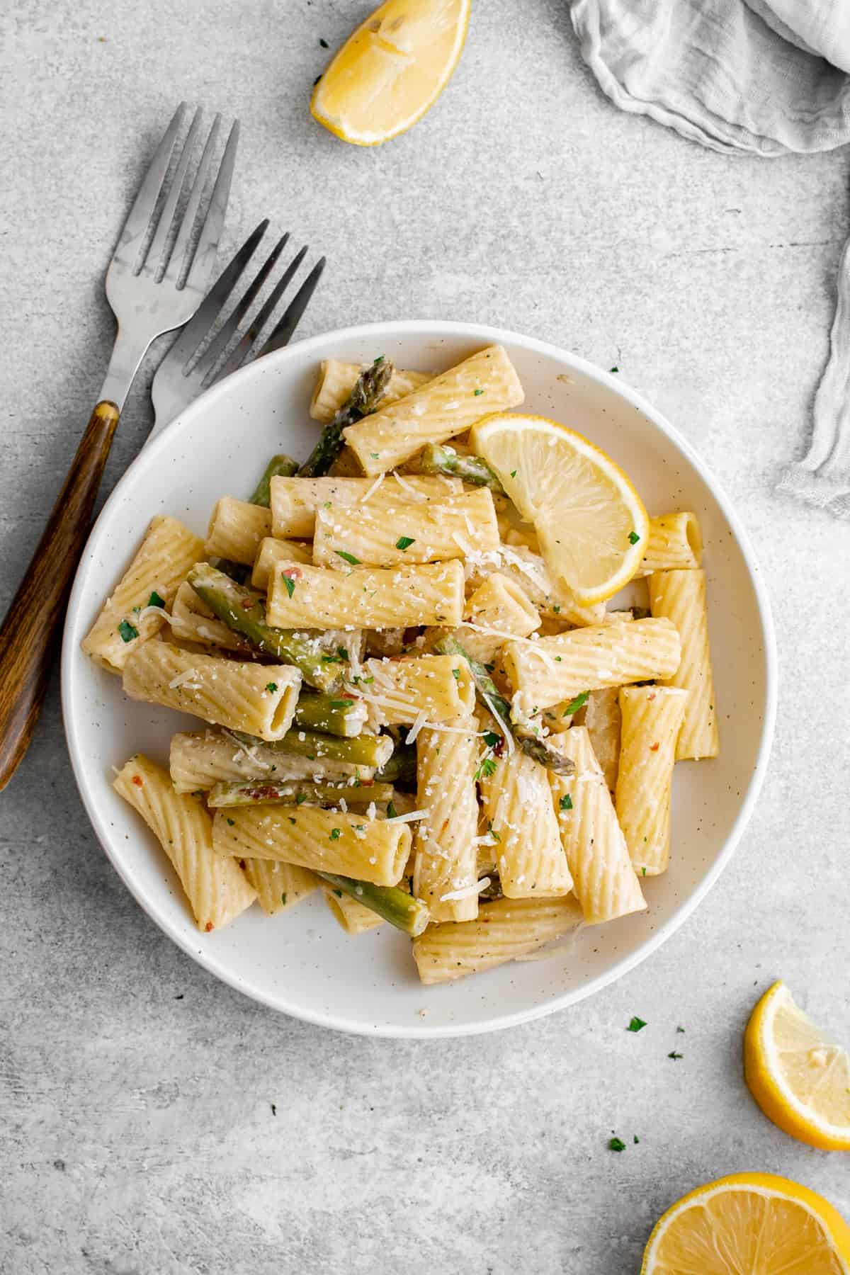 overhead view of a bowl of lemon asparagus pasta with forks and lemon slices scattered around