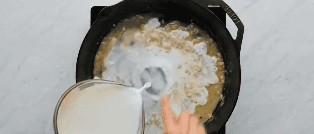 Pouring milk into a skillet with flour, garlic and butter. 