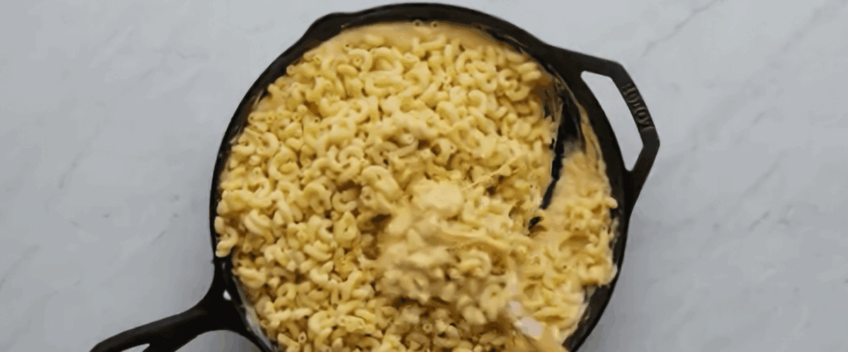 Adding pasta to the skillet with the cheese sauce. 