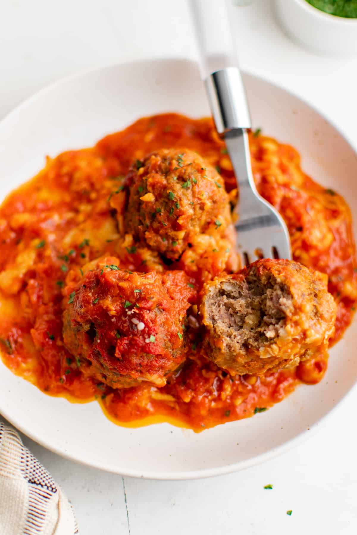 a plate of cheesy meatball casserole with a bite taken out of it.