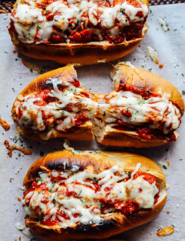 overhead view of meatball subs on a lined baking sheet, one cut in half.