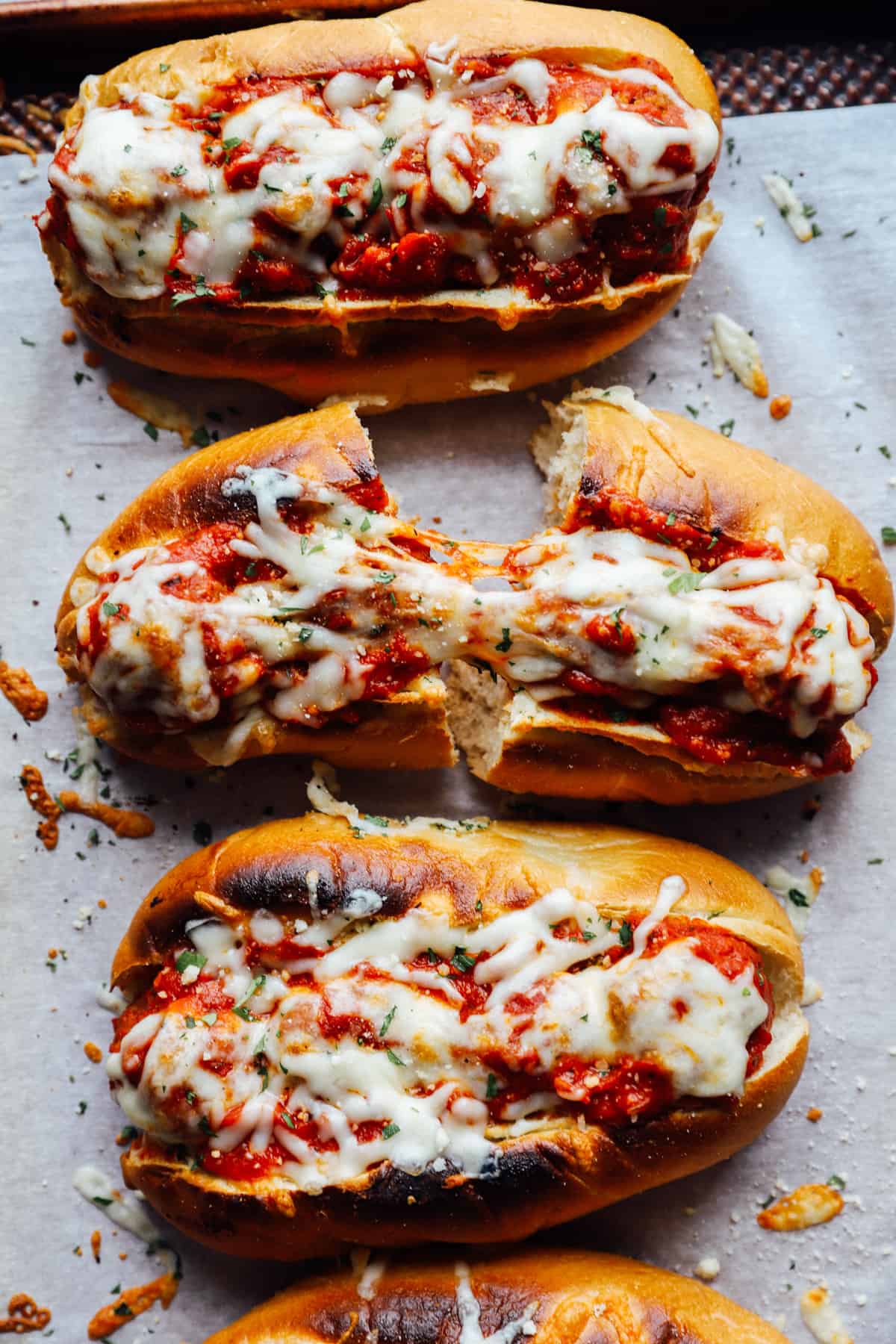 overhead view of meatball subs on a lined baking sheet, one cut in half.