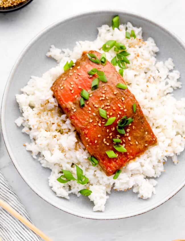 overhead view of miso glazed salmon on a bed of white rice on a white plate.