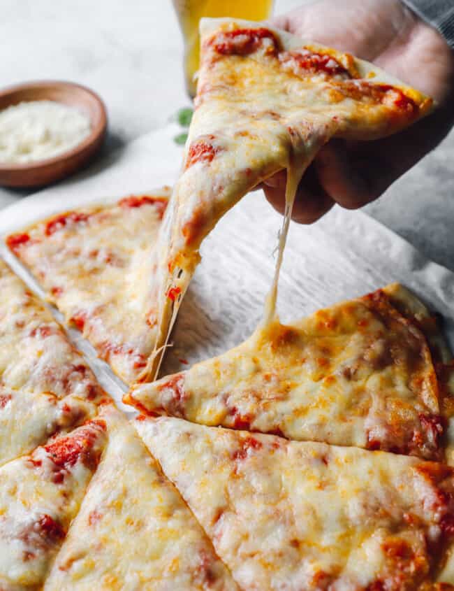 a hand grabbing a slice of new york pizza from a cut pie.