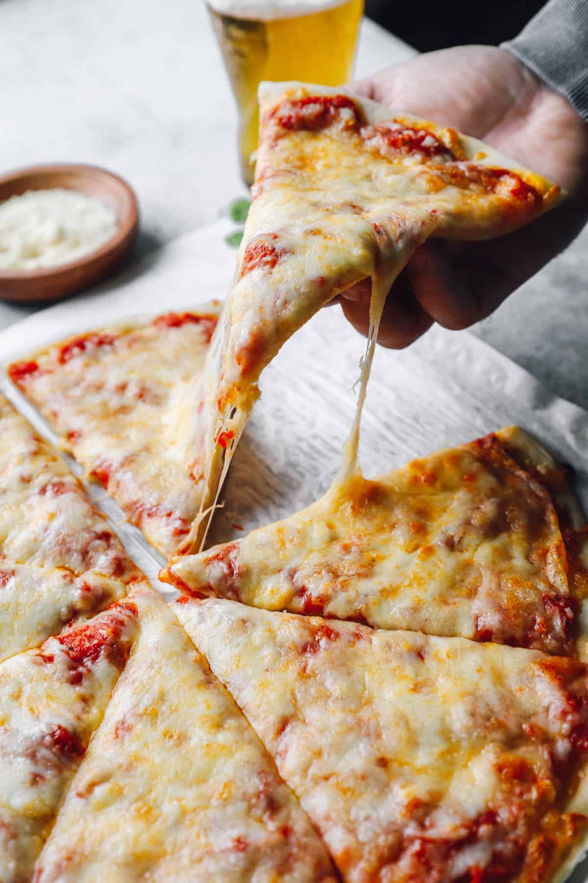 a hand grabbing a slice of new york pizza from a cut pie.