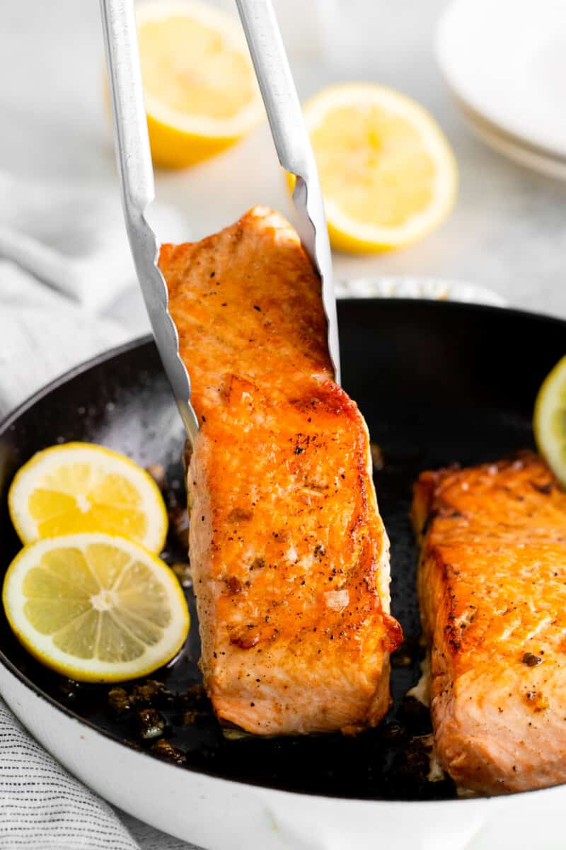 tongs grabbing a salmon filet from a cast iron pan.