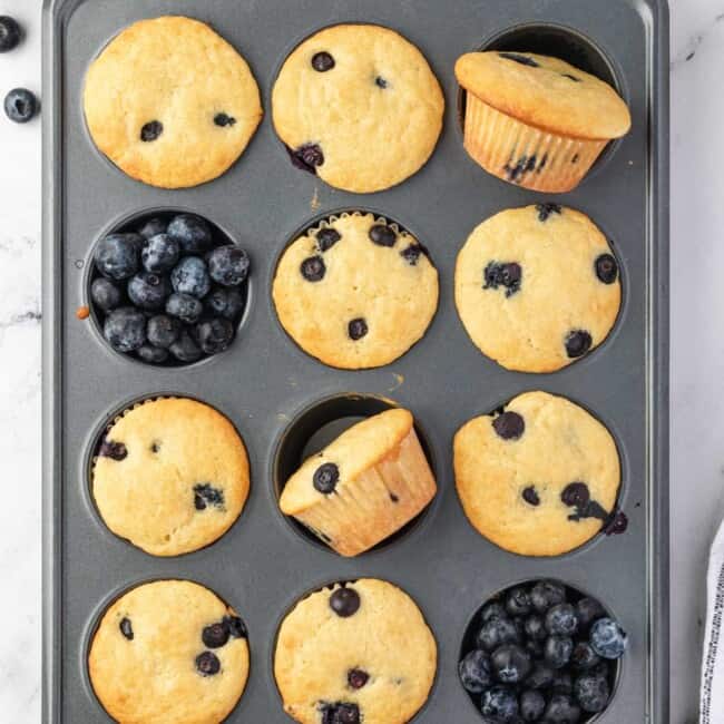 10 blueberry pancake muffins in a muffin tin with blueberries in the remaining muffin wells.