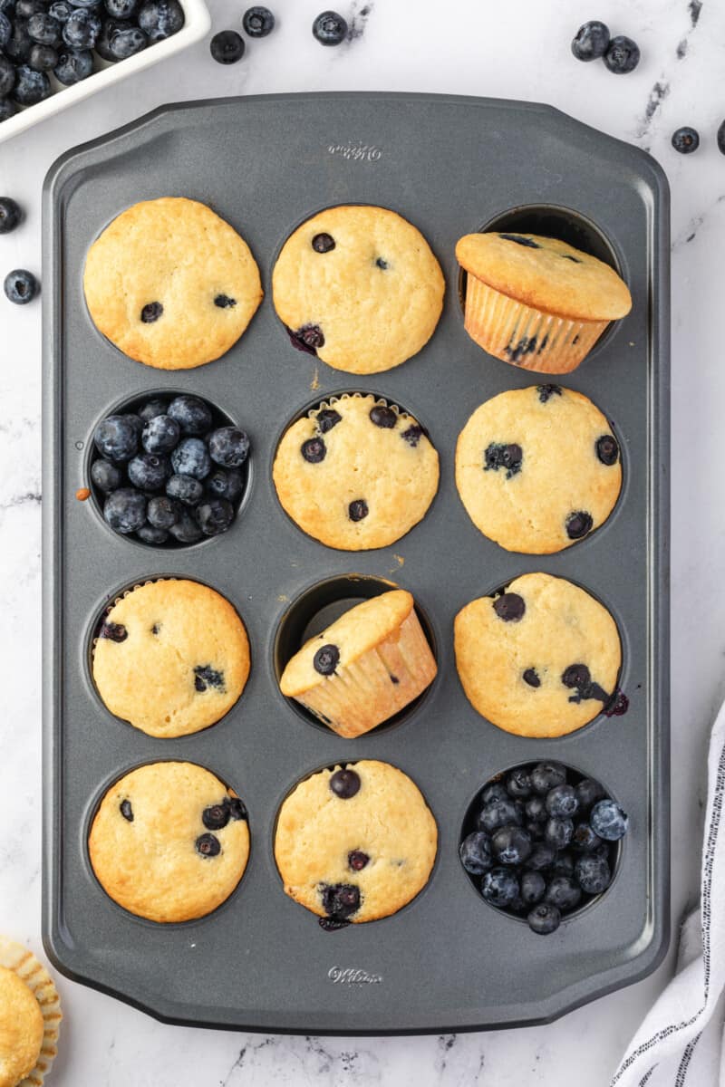 10 blueberry pancake muffins in a muffin tin with blueberries in the remaining muffin wells.