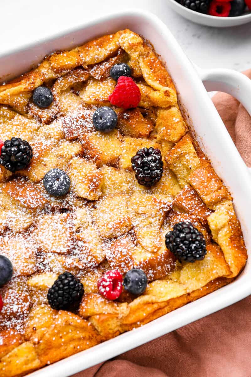 bread pudding in a white baking pan with powdered sugar and berries.