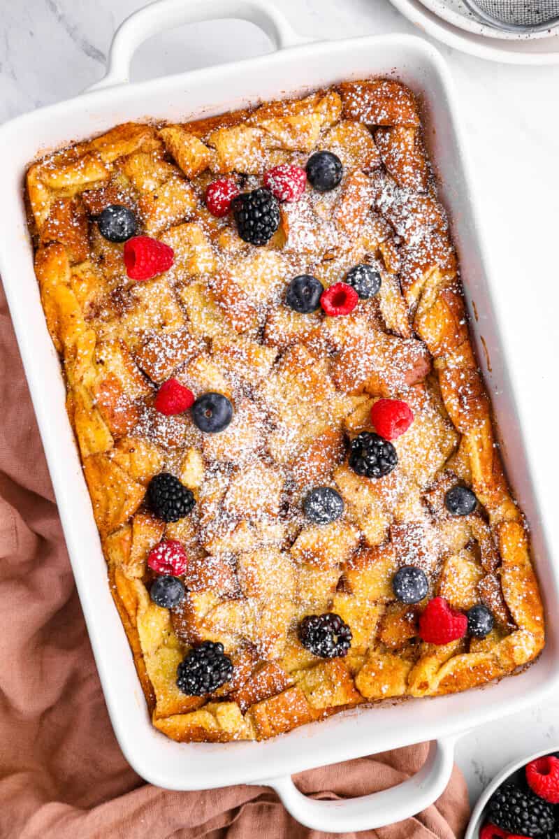 overhead view of bread pudding in a white baking pan with powdered sugar and fresh berries.