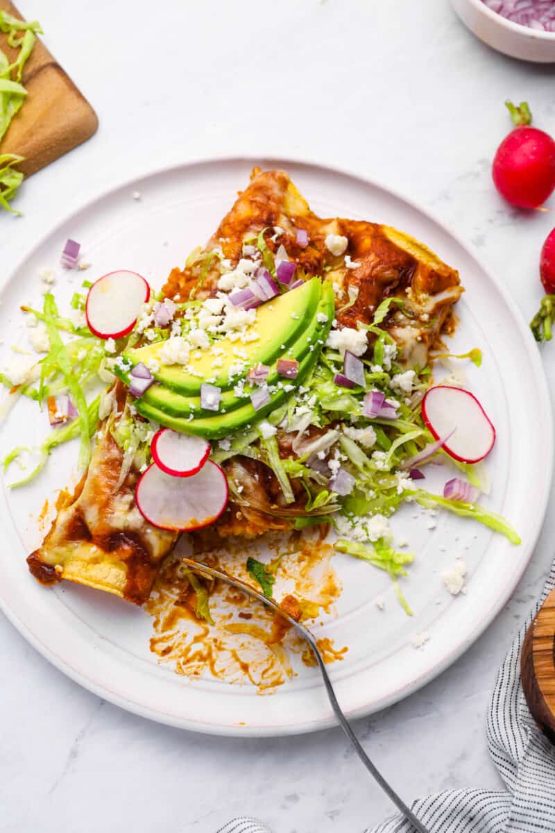 2 chicken enchiladas on a white plate with lettuce, radish, onion, and avocado.