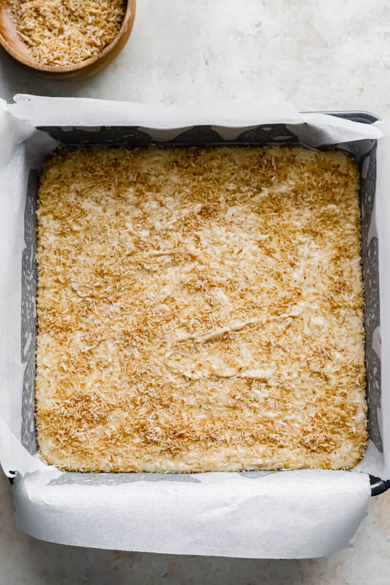 coconut fudge topped with toasted coconut in a square baking pan.