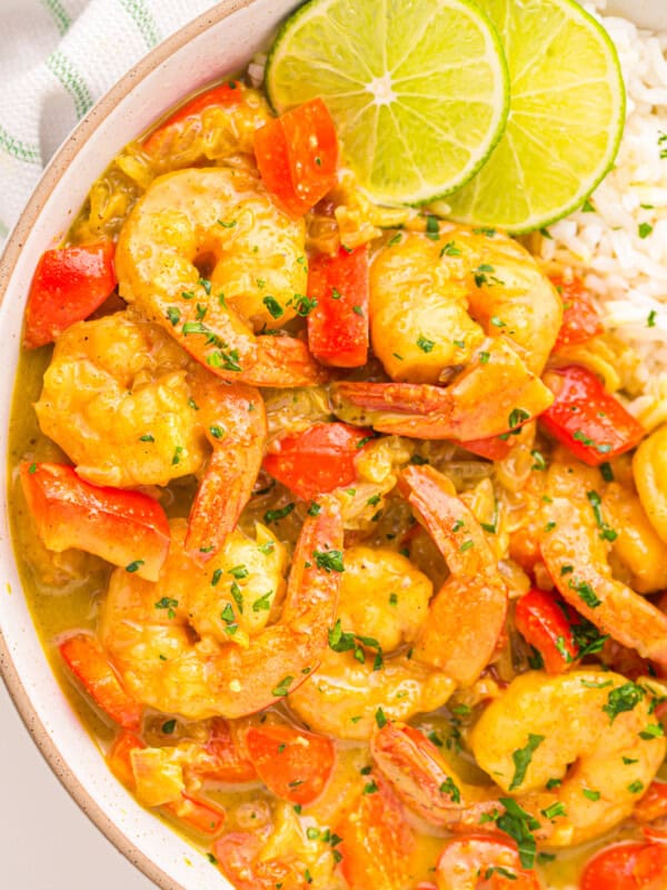 overhead partial view of coconut curry shrimp in a white bowl with rice and lime wedges.