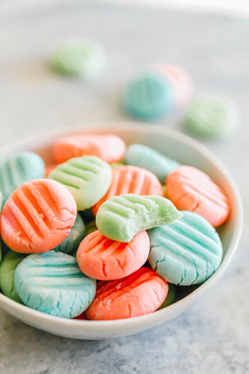 a bitten green cream cheese mint resting on top of cream cheese mints in a white bowl.