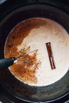 overhead view of ingredients for crockpot eggnog in a slow cooker with a whisk.