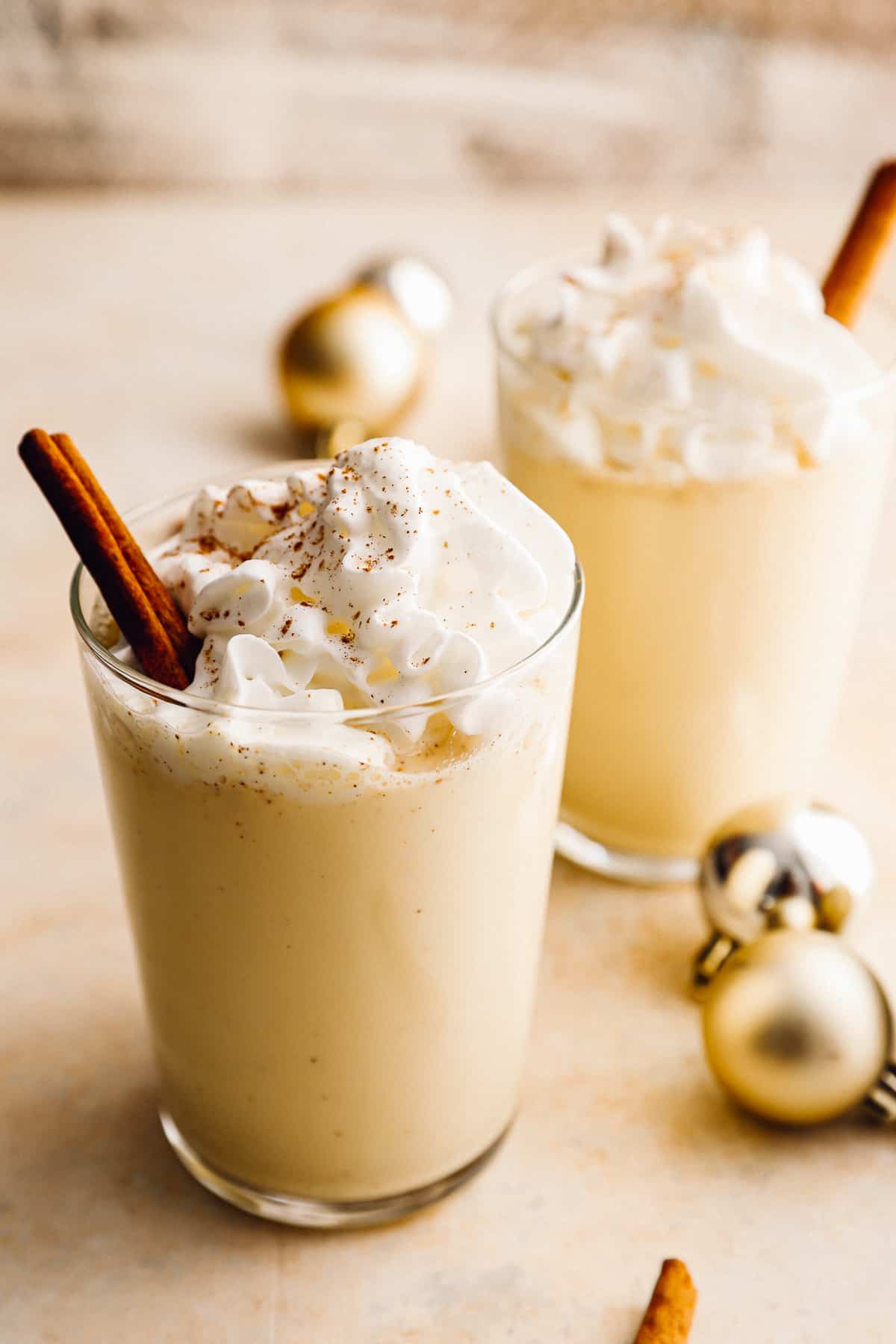 2 glasses of crockpot eggnog with whipped cream and cinnamon sticks.