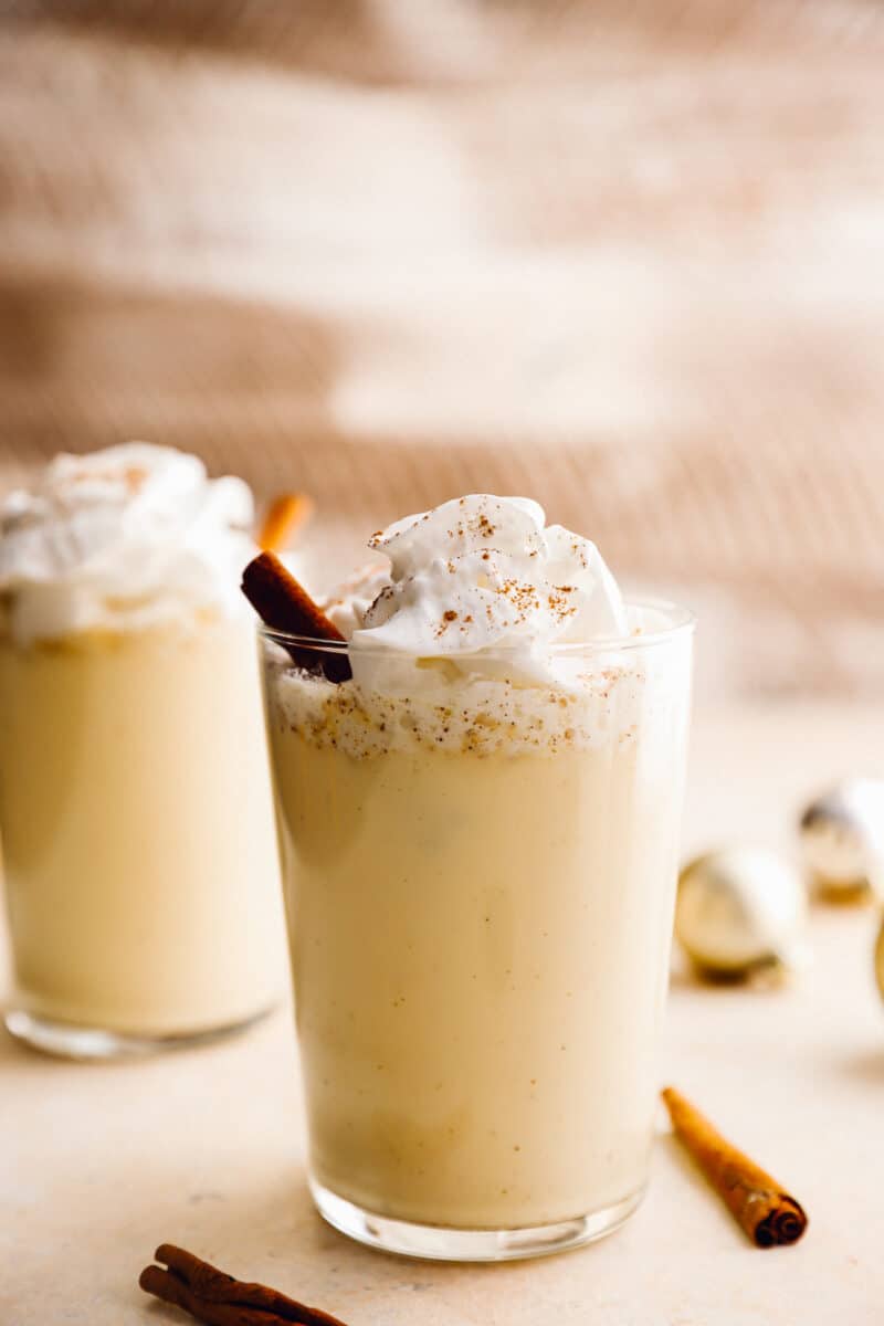 2 glasses of crockpot eggnog with whipped cream and cinnamon sticks.