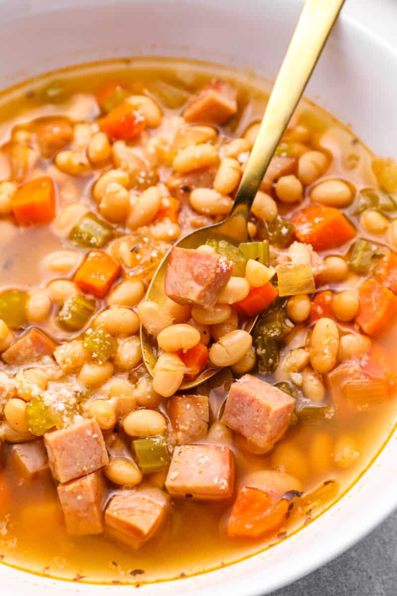 close up of crockpot ham and bean soup in a white bowl with a spoon.