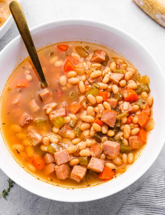 crockpot ham and bean soup in a white bowl with a spoon.