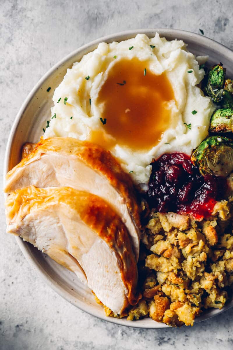 deep fried turkey slices on a white plate with stuffing, mashed potatoes, gravy, brussels sprouts, and cranberry sauce.