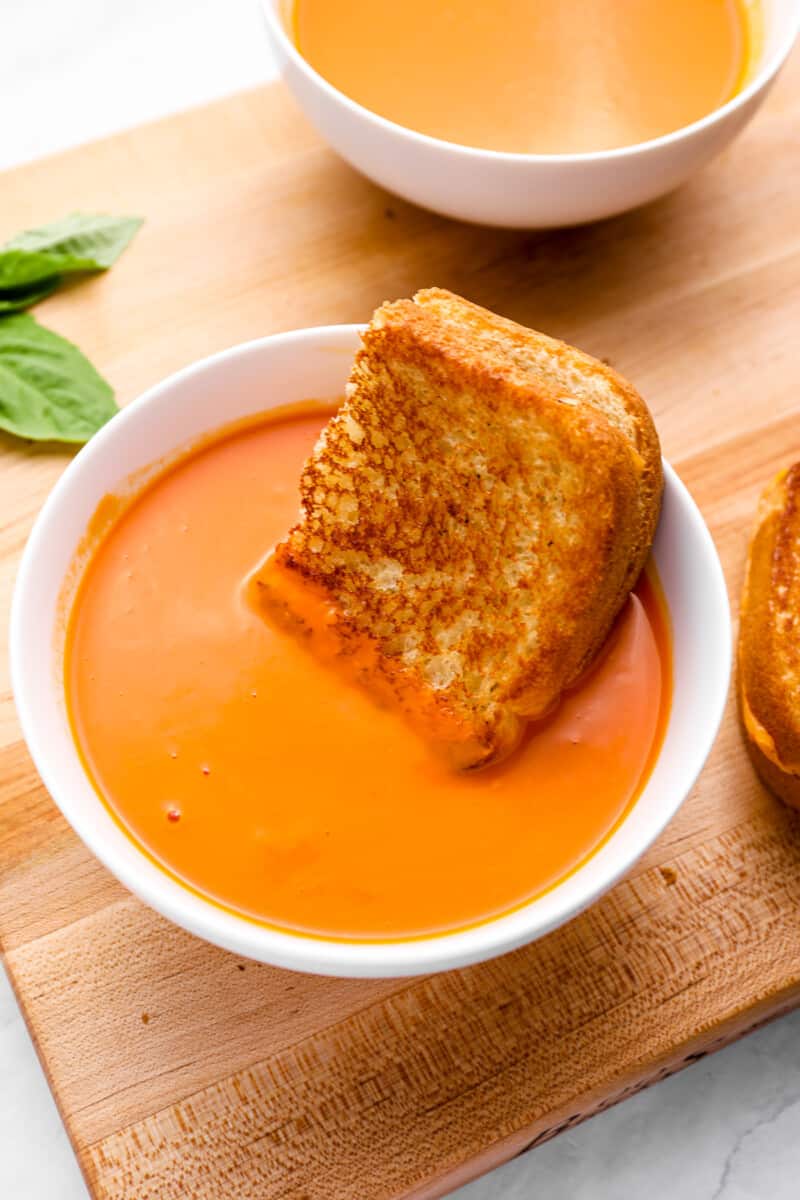 half of a grilled cheese dipped in a bowl of tomato soup.