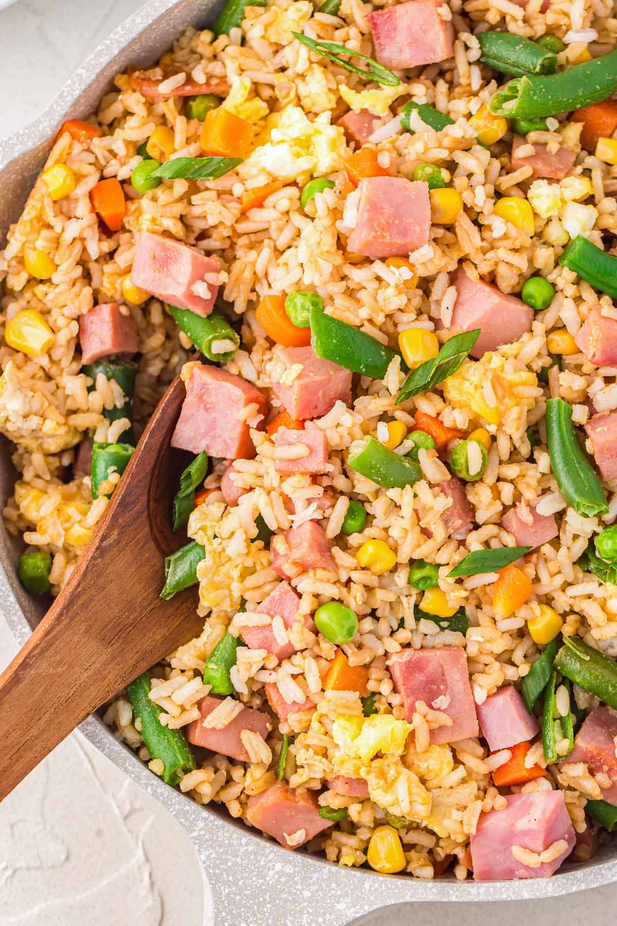 ham fried rice in a frying pan with a wooden spoon.