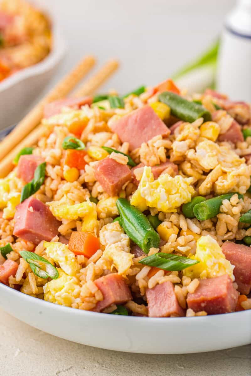 close up of ham fried rice in a white bowl with chopsticks.