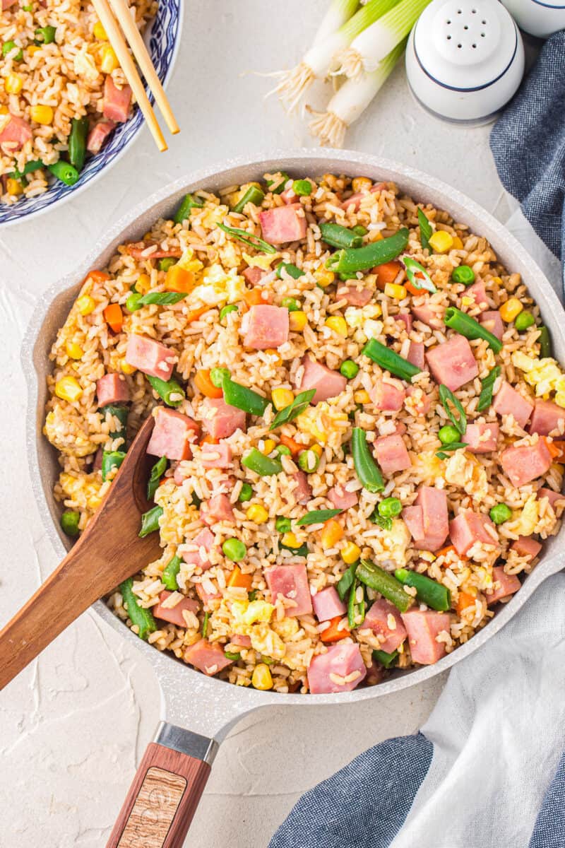 overhead view of ham fried rice in a white bowl with a wooden spoon.