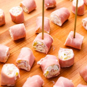skewered ham roll ups on a wooden cutting board.