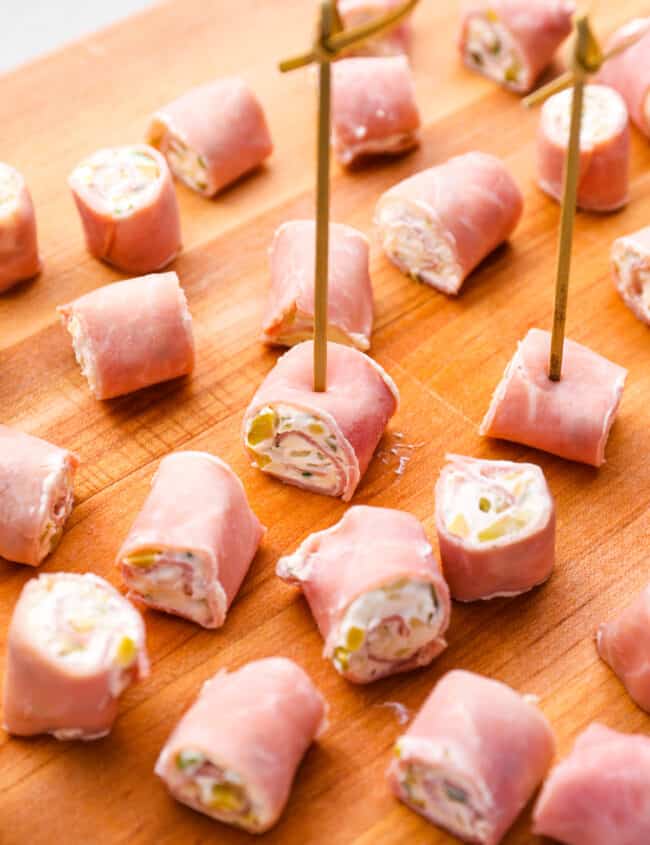 skewered ham roll ups on a wooden cutting board.