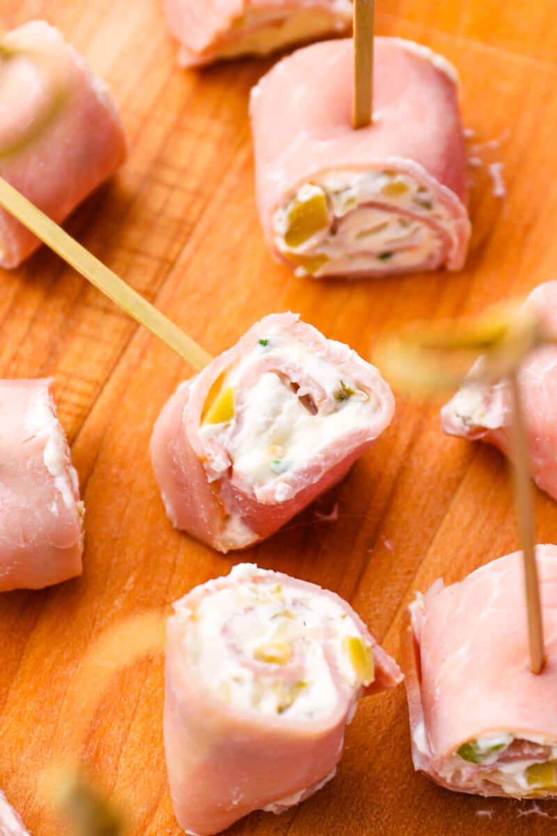 close up of skewered ham rolls on a wooden cutting board.