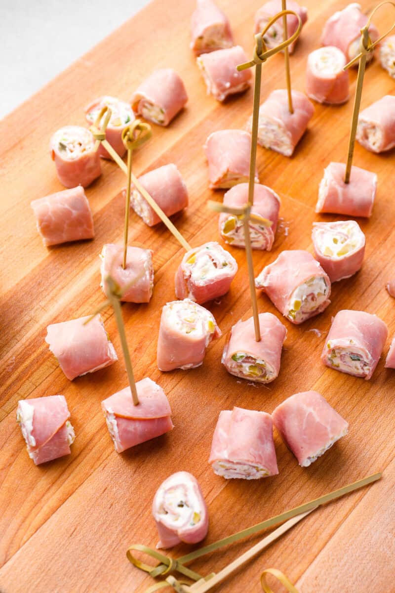skewered ham rolls on a wooden cutting board.