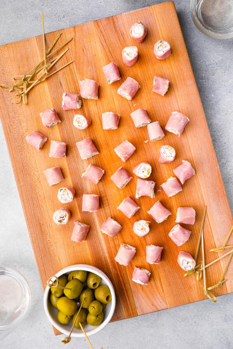 ham roll ups on a wooden cutting board with a side of pickles.
