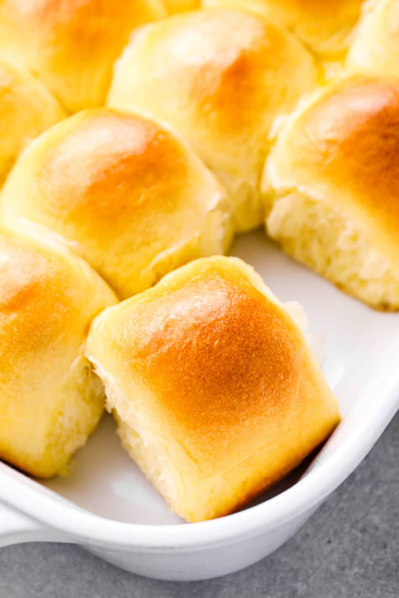 close up of dinner rolls in a white baking dish, one has been removed.