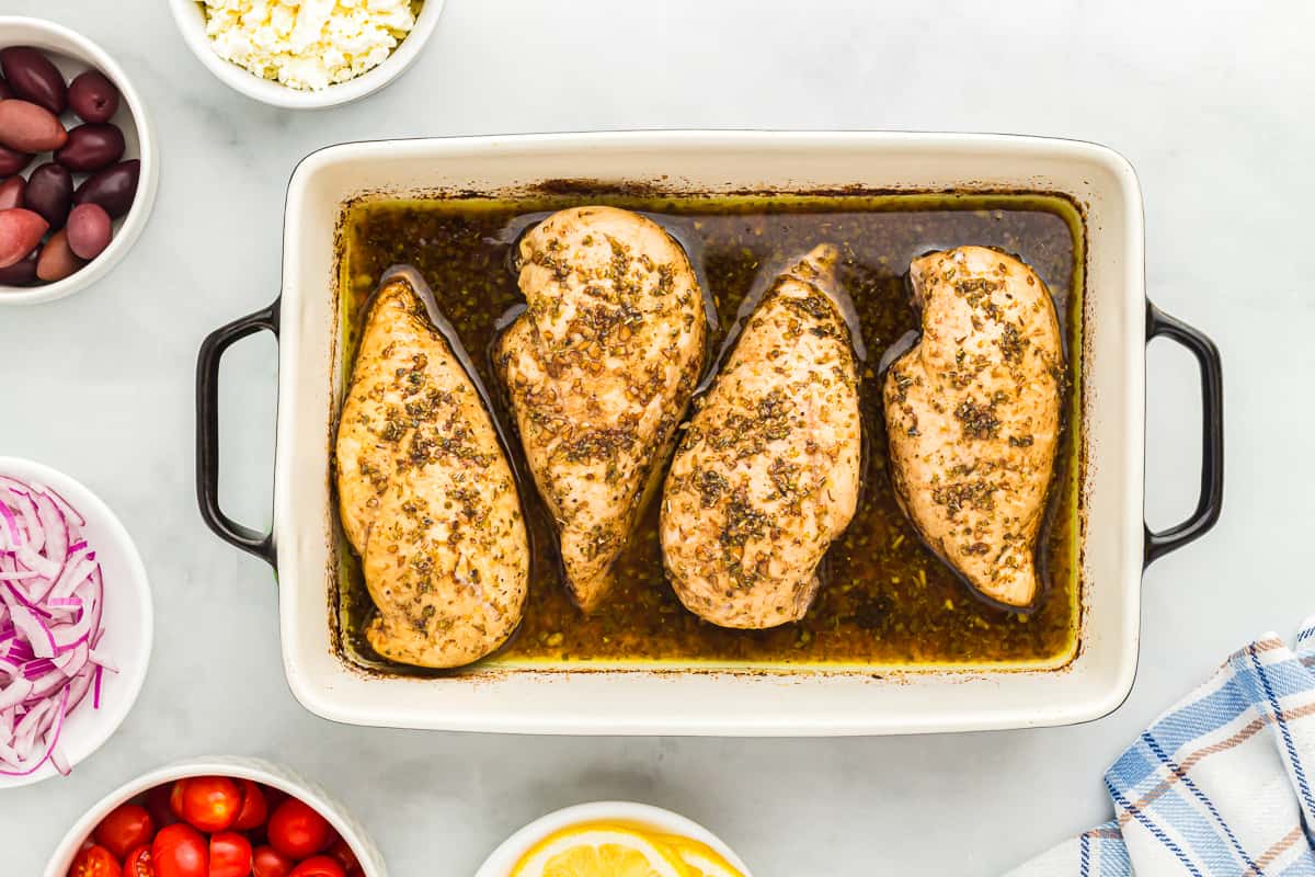 4 baked greek chicken breasts in a rectangular baking dish.