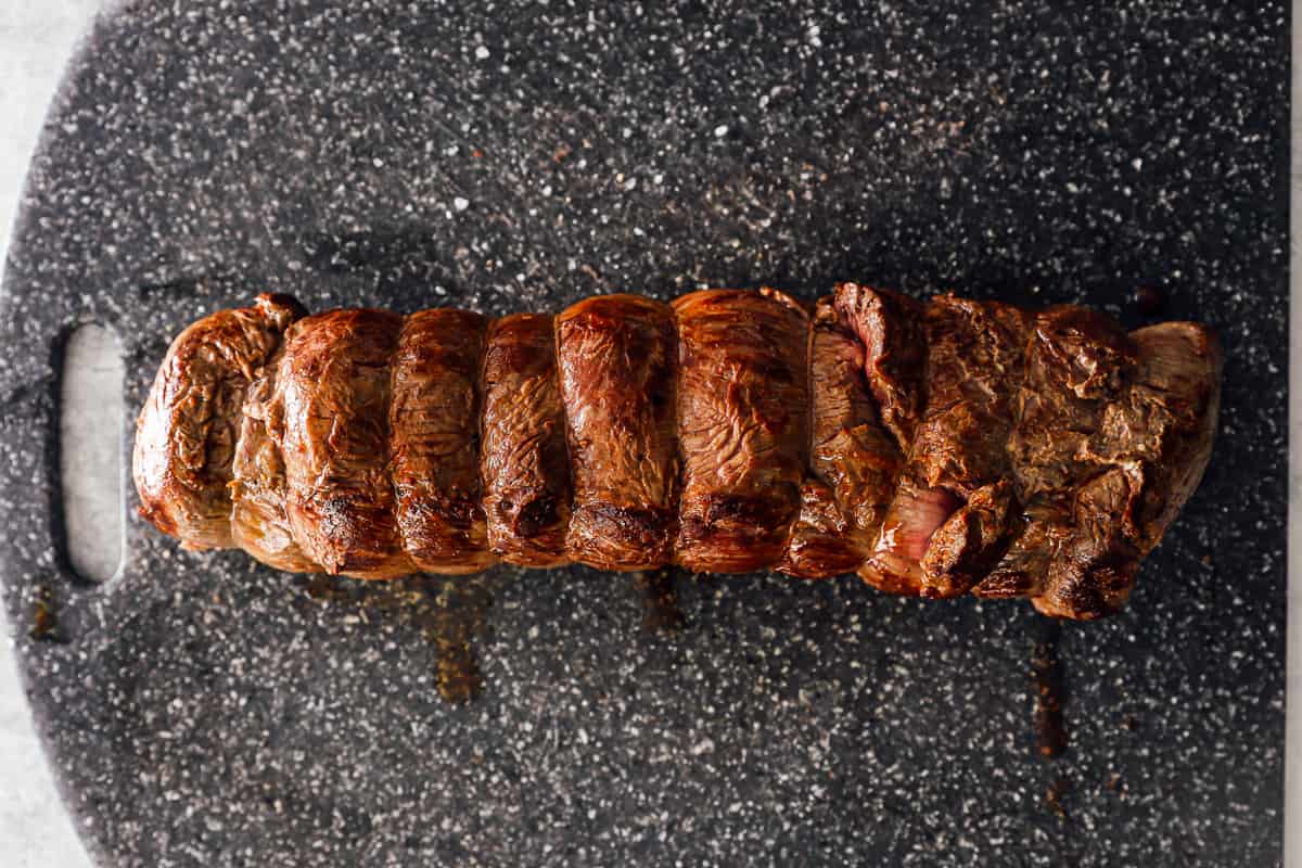 seared beef tenderloin wrapped in twine on a gray cutting board.