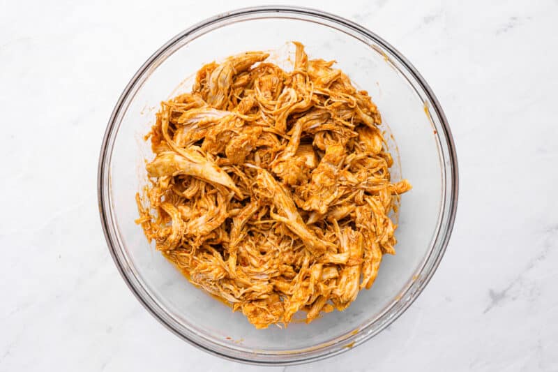 shredded chicken coated in enchilada sauce in a glass bowl.