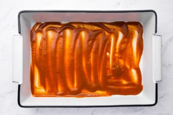 enchilada sauce spread in a thin layer on the bottom of a rectangular baking pan.