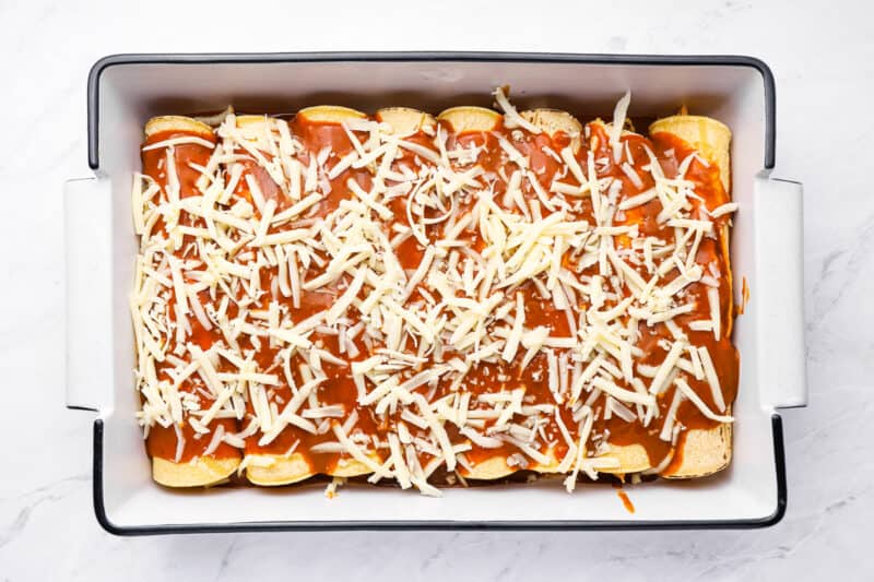 8 rolled up chicken enchiladas topped with sauce and shredded cheese.